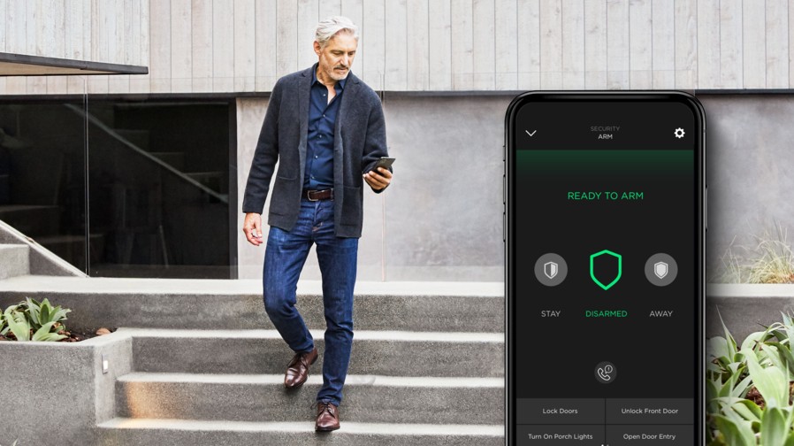A man walks down stairs while using a smartphone to manage a Savant home security mobile app interface.